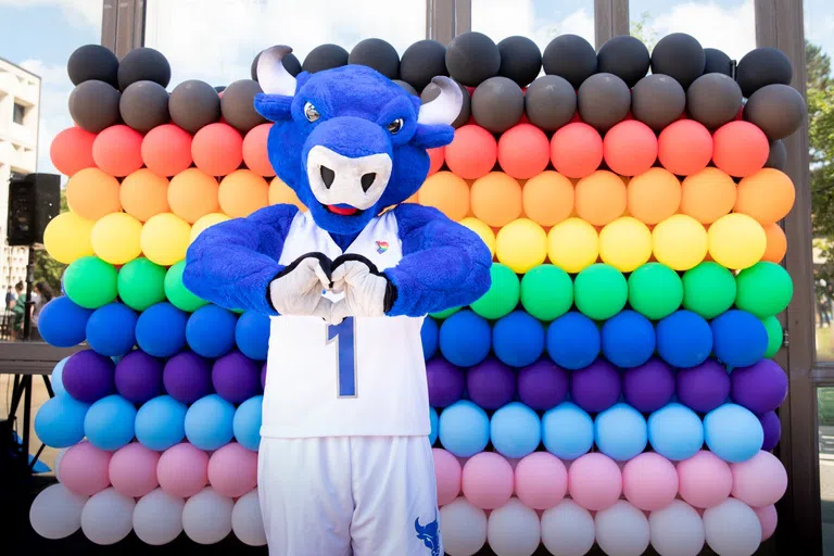 UB mascot, Victor E. Bull, standing in front of rainbow balloons