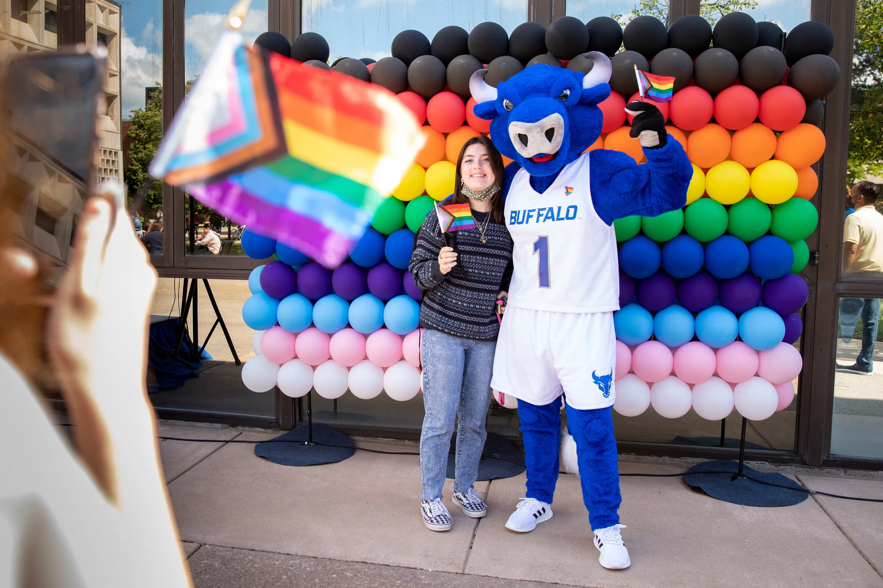 UB mascot, Victor E. Bull, posing with student in front of rainbow balloons