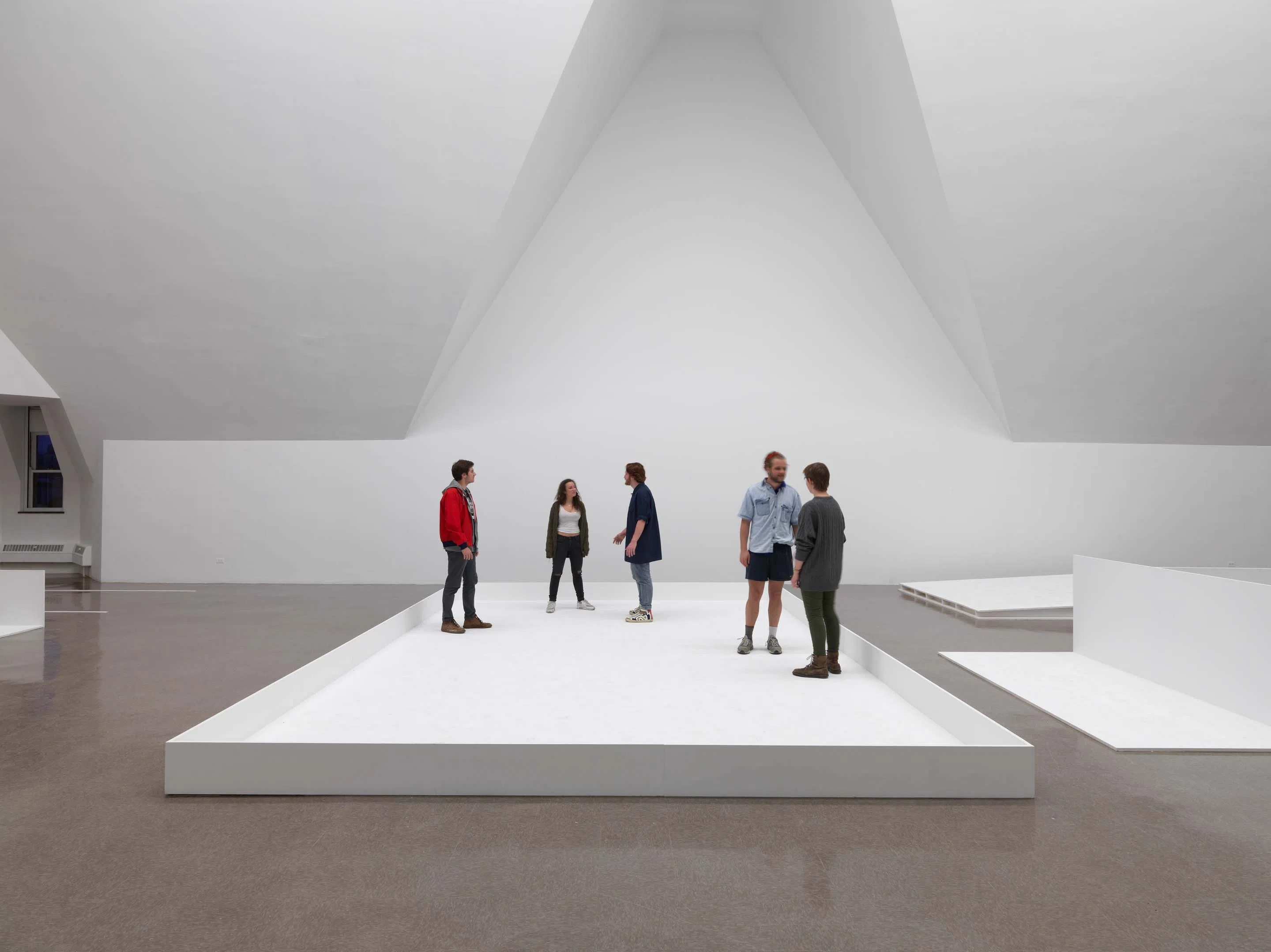 5 students stand on a white platform in an empty white art museum space with cathedral ceilings