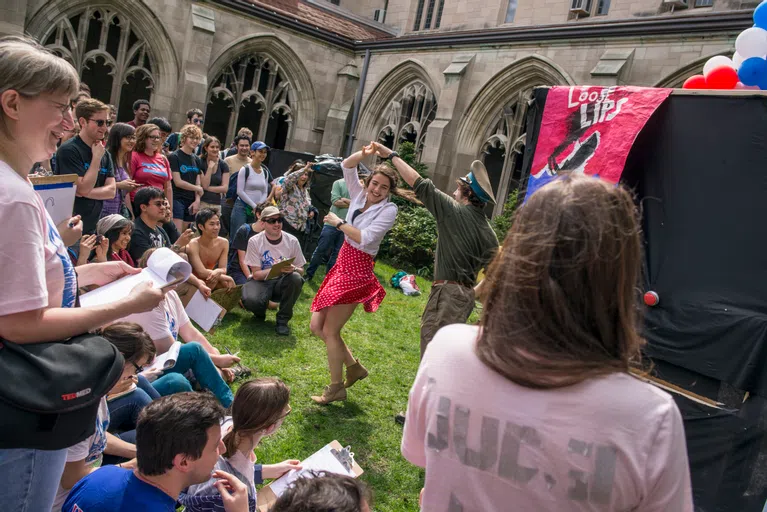 Students dance in front of a cheering outdoor crowd in a courtyard