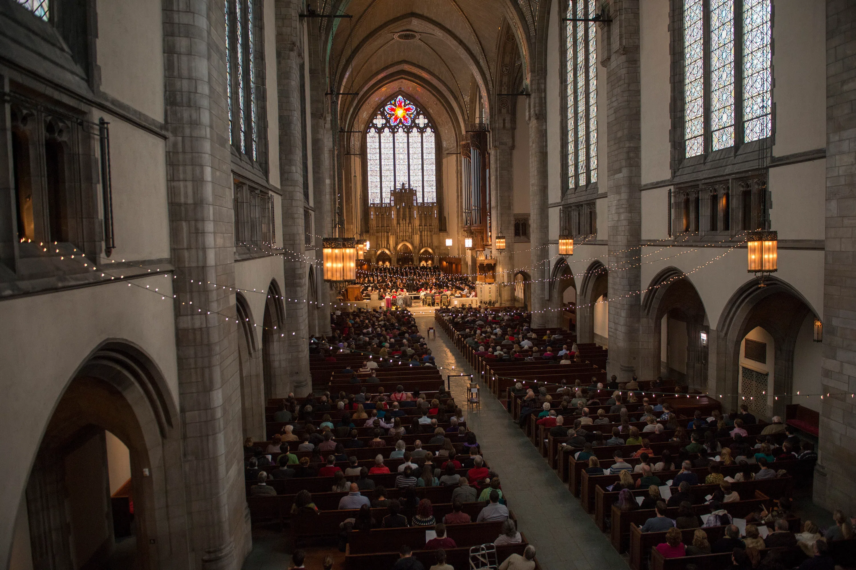 Rockefeller Chapel interior with large crowd in pews, string lights hanging overhead, choir on stage