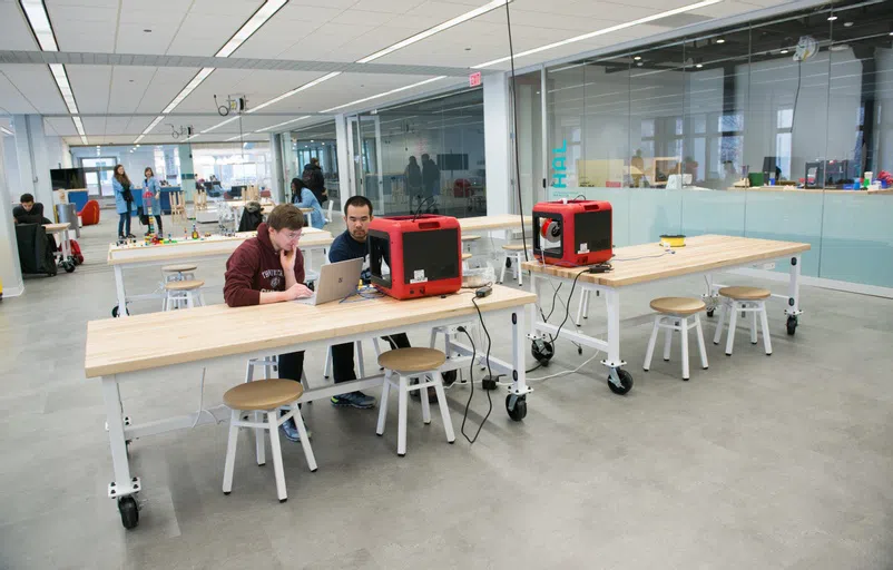 two students working on a 3D printer in the MADD lab