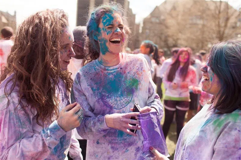 3 students smile, covered with colored powder after a campus Holi celebration