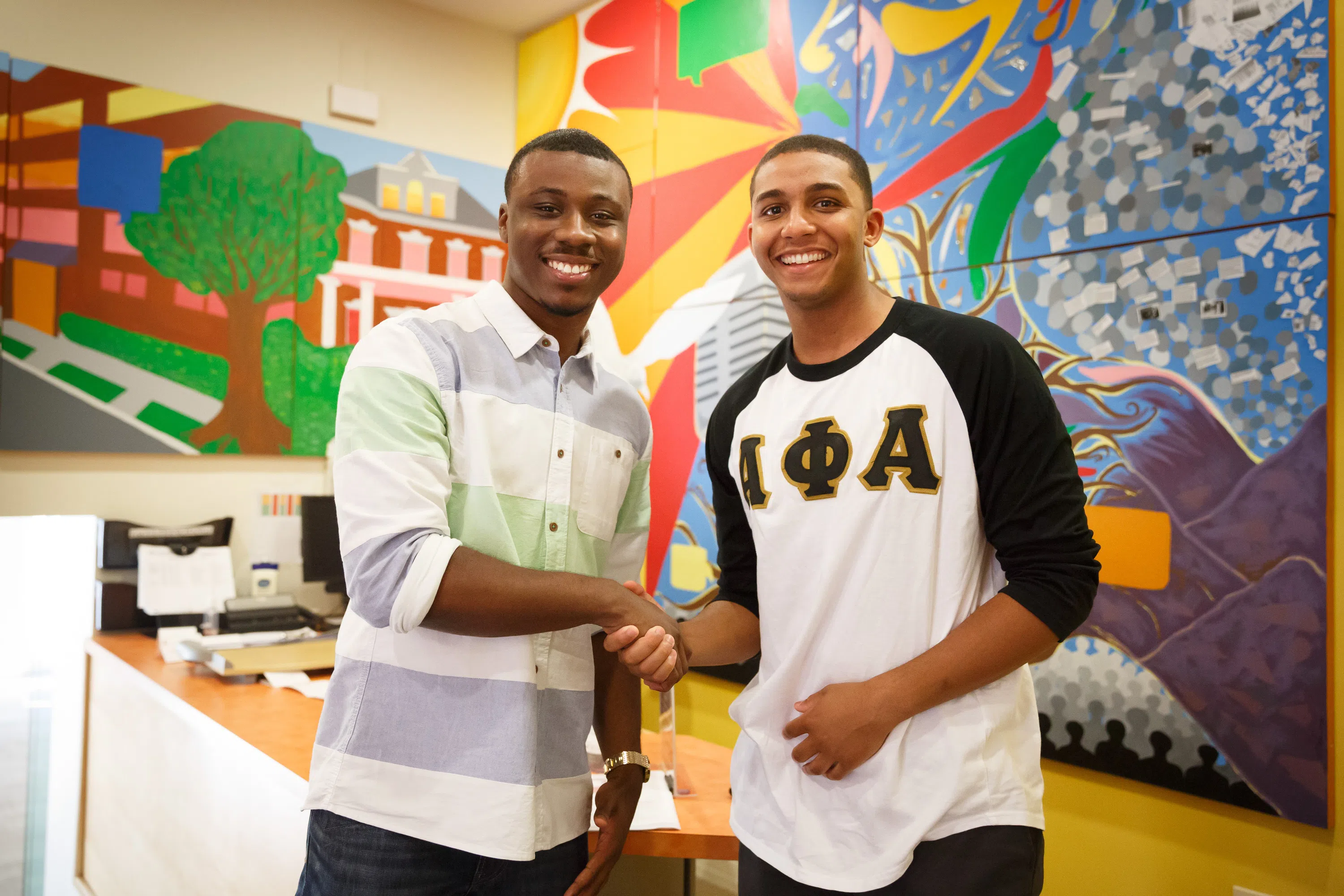 Two students shake hands, smiling at the camera