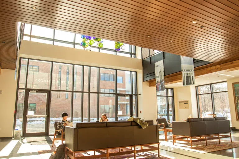 Two students sit studying on a couch that is in a large sunny room with many windows