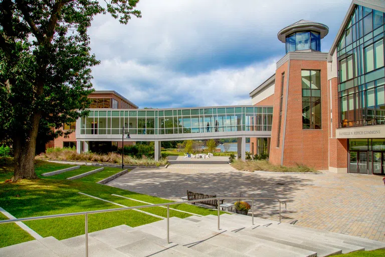 Large brick building with a bridge and wall-to-wall windows. Waterview in the background