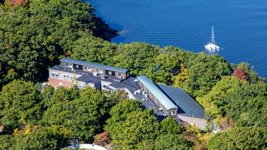 aerial shot of a long building surrounded by trees and near the water