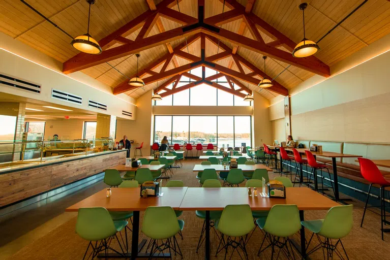 large room with chairs and table. Food serving station on left. Wall covered windows in back