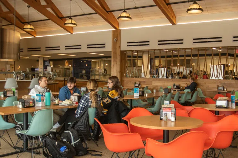 group of four students sit at a dining table with colorful teal and orange chairs