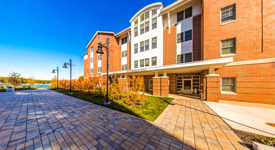 Sunny brick building with a stone walkway. Waterfront is visible in the background