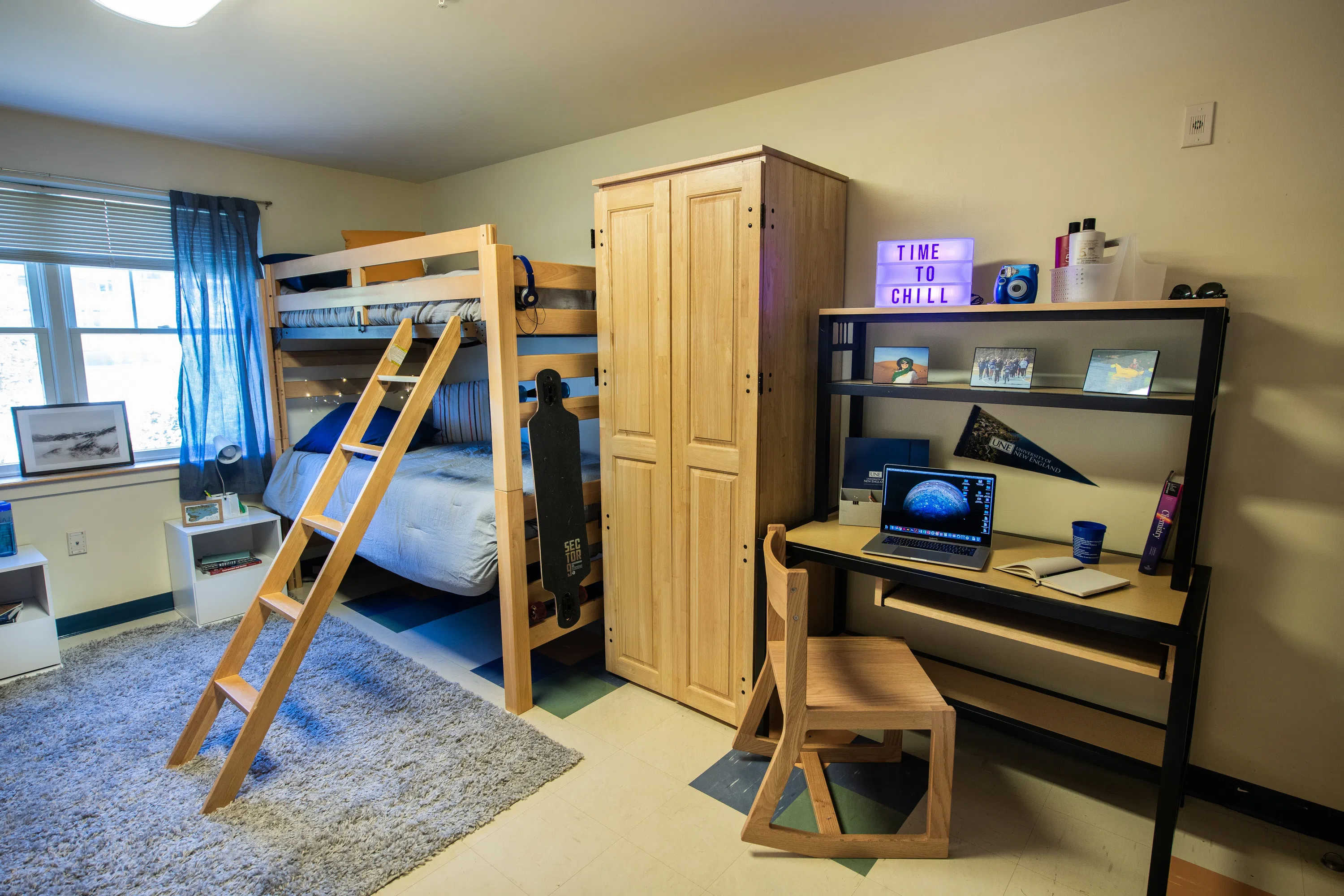 A wooden bunk bed with a ladder is on the left side of the room. Right side has a dresser and desk. 