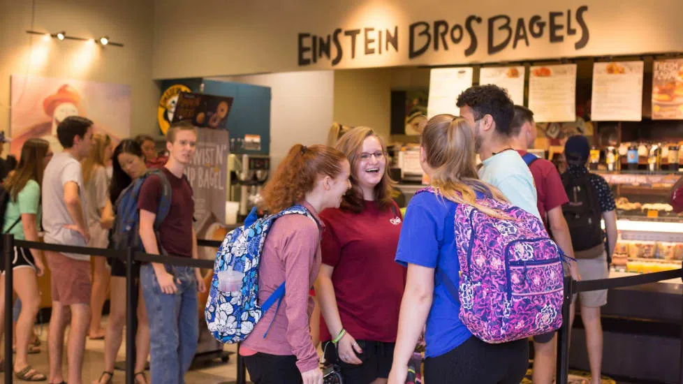 Group of students laughing together while waiting in line for Einstein Bros. Bagels