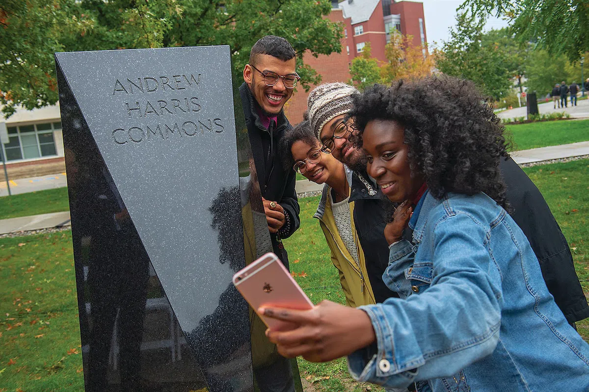 Students taking a selfie with the Andrew Harris Commons black marble marker.