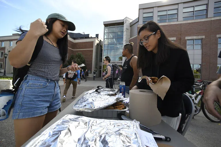 Two students standing outside next to a table of food.