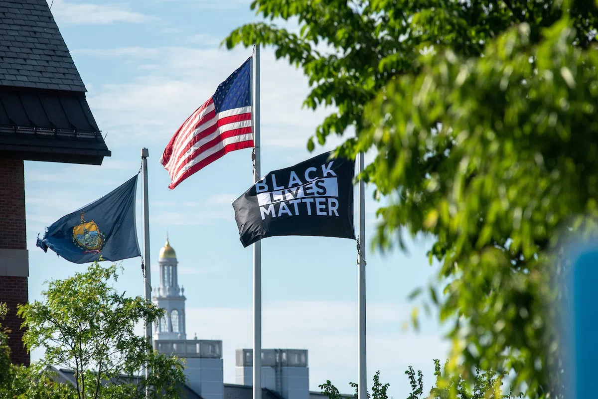 Black Lives Matter Flag flying with US and Vermont flags with UVM buildings behind them.