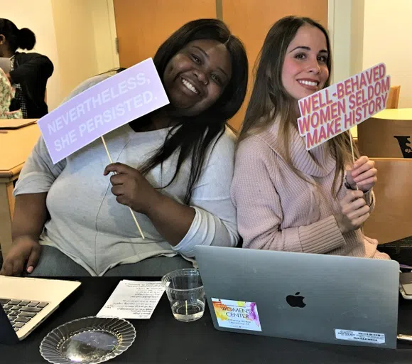 Two Vanderbilt students show signs reading "Nevertheless, she persisted" and "well-behaved women seldom make history" at a Women's Center event.