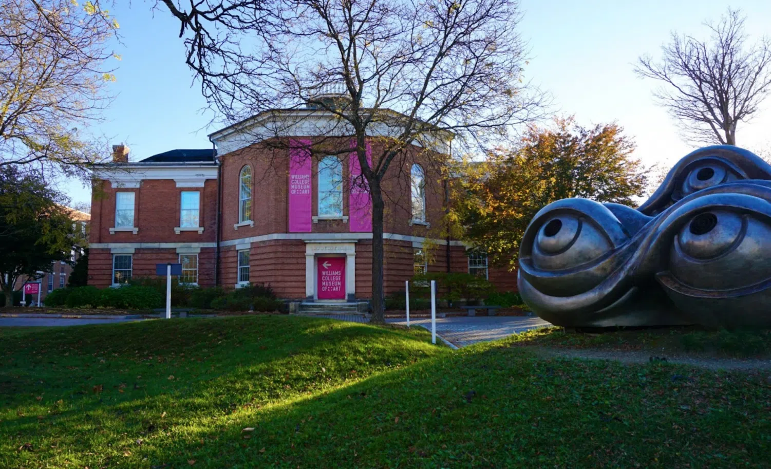 The Williams College Museum of Art, a rounded red brick building, with a sidewalk and grass in front of it, and a sculpture of eyes.
