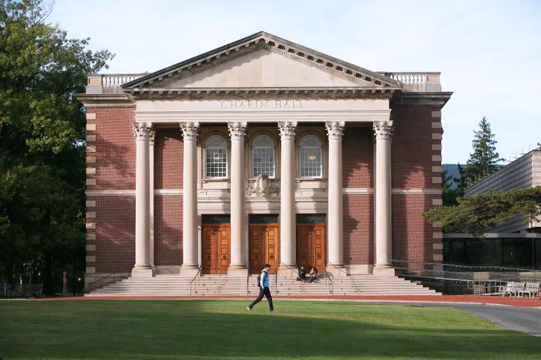 A student walking in front of Chapin Hall, a red brick and white stone building with steps and six columns.