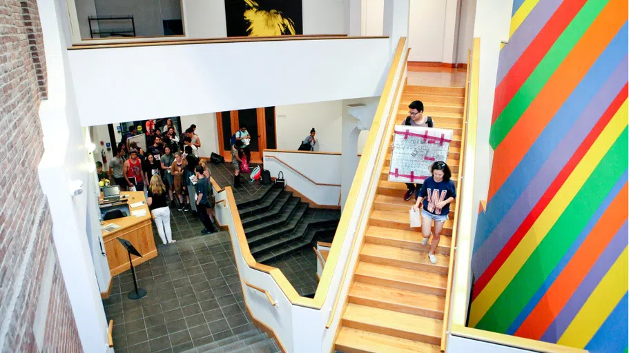 students walking with loaned art pieces down stairs of WCMA interior