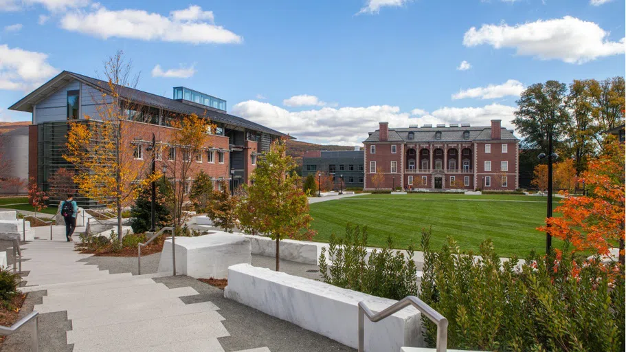 An image of Sawyer Quad, with marble benches in the foreground, a grassy quad area, Hollander Hall on the left, and Sawyer Library in the background.